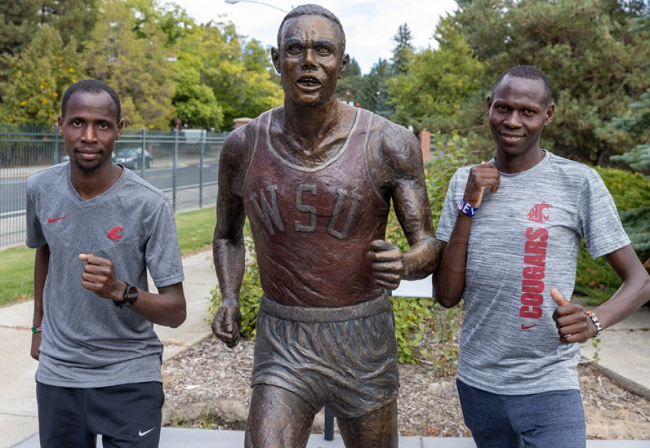 Kenyan students at Washinton State University also athletes pose at the statue of Henry Rono og image
